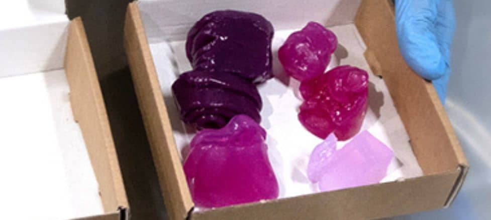 Colorful 3D printed structures in a cardboard box, handled with blue gloves.