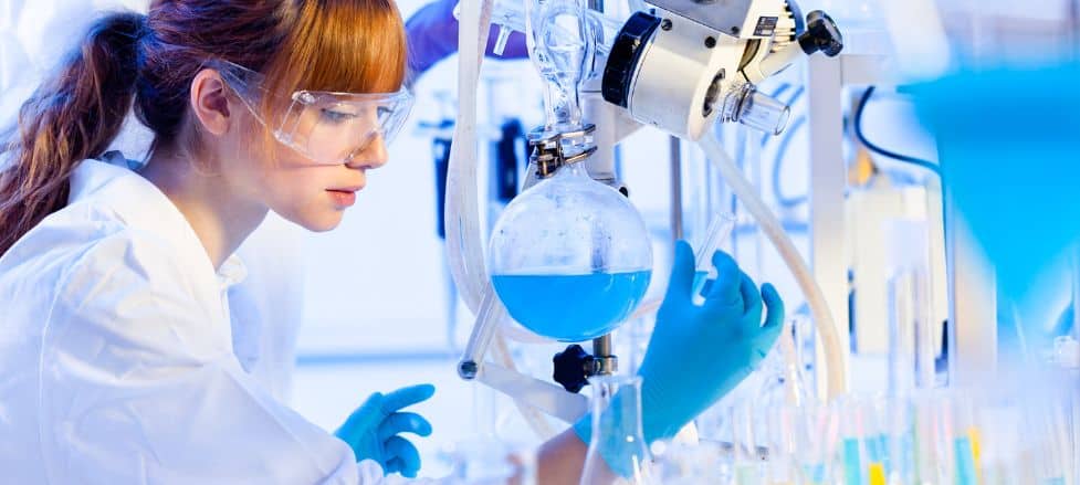 Female scientist conducting an experiment in a laboratory with blue liquid in glass equipment.