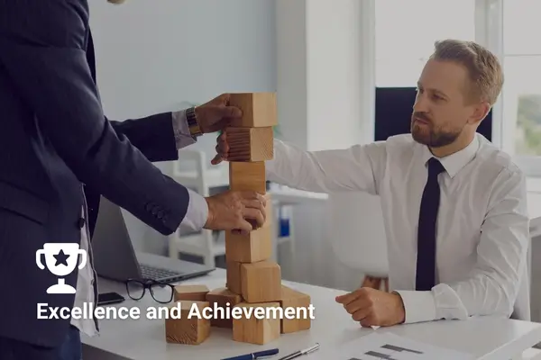 Business teamwork and strategy, two men building a block tower in an office setting with a trophy icon symbolizing success.