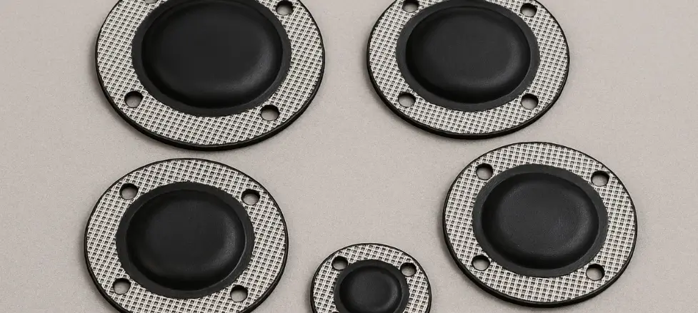 Round black rubber gaskets with metal edges, arranged on a beige surface.